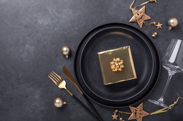 Cadre de table de Noël avec assiette en céramique noire, verre, coffret cadeau et accessoires dorés sur fond de pierre noire. Vue de dessus. Espace de copie - Image