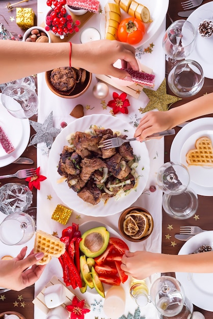 Photo cadre de table de noël avec de la nourriture sur une assiette, maman et enfant mains remettant des aliments et de la décoration sur une table en bois sombre, plat poser