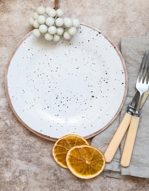 Cadre de table de vacances d'hiver Assiette en céramique artisanale, serviettes en lin, couverts et tranches d'oranges sèches