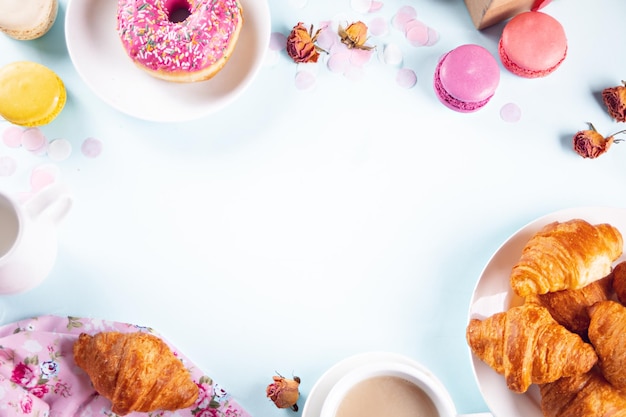 Cadre avec tasse de thé, croissants frais, macarons, beignets. Concept de mode de vie sain. Style romantique. Vue de dessus. Copiez l'espace.