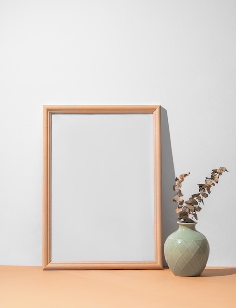 Un cadre avec une toile blanche contre un mur léger et sur une table en bois avec un vase