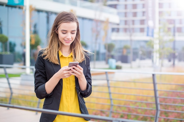 Cadre travaillant avec un téléphone portable dans la rue avec des immeubles de bureaux