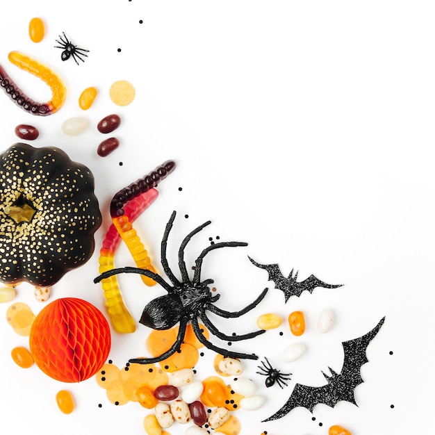 Cadre de vacances d'Halloween avec des bonbons colorés, des chauves-souris, des araignées, des citrouilles et une décoration sur fond blanc. Mise à plat. Vue d'en-haut
