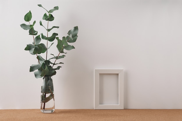 Cadre et vase à l'eucalyptus sur un mur blanc