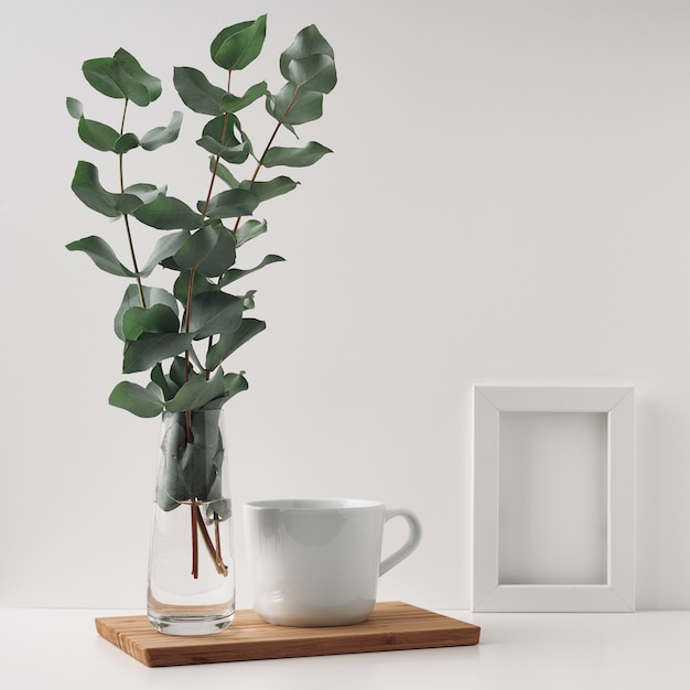 Cadre, vase à l'eucalyptus et une tasse sur une planche de bois