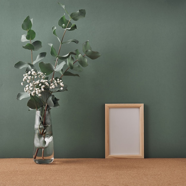 Cadre et vase à fleurs blanches et eucalyptus sur un mur vert foncé