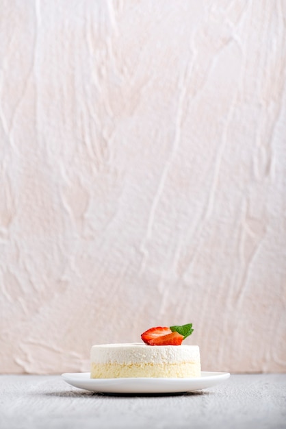 Cadre vertical. Cheesecake aux fraises sur plaque blanche sur fond clair. Vue de côté.