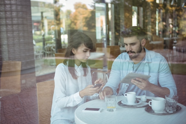 Cadres utilisant un téléphone mobile et une tablette numérique dans une cafétéria