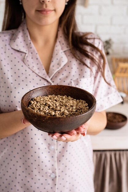 Café alternatif brassant une jeune femme en joli pyjama faisant du café à la cuisine à la maison tenant un bol avec des grains de café