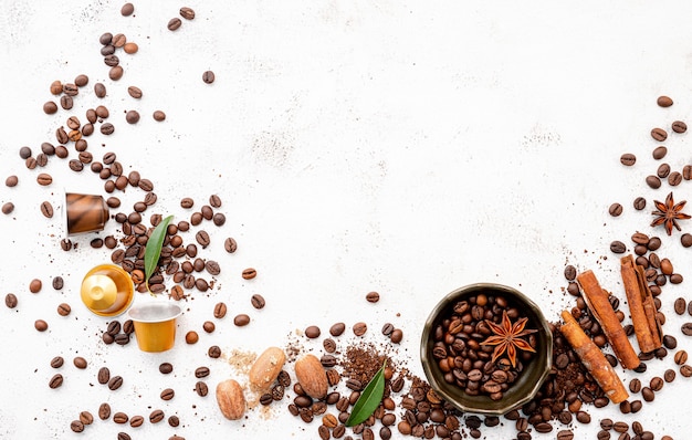 Café arious, grains de café torréfiés foncés, moulu et capsules avec cuillères sur béton blanc