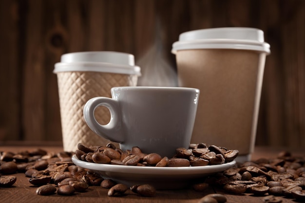 Café aromatisé chaud et frais. Tasse à café fumante et gobelets en papier. Sur Fond En Bois Vintage Avec Des Grains De Café.