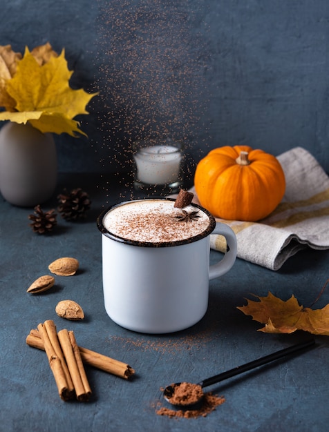 Café au lait aux épices sur une tasse blanche avec de la citrouille, de la cannelle et des noix sur la table bleu foncé