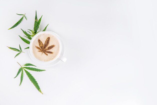 Café au lait de chanvre médical Coupe de café fouetté crémeux avec des gouttes d'huile de cannabis et des feuilles dessinées sur le dessus avec des feuilles de chanvre sur fond blanc