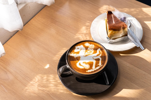 Café au lait chaud avec art latte sous la forme d'une mousse de lait de jument dans une tasse et un gâteau au chocolat fait maison sur un bureau en bois en vue de dessus