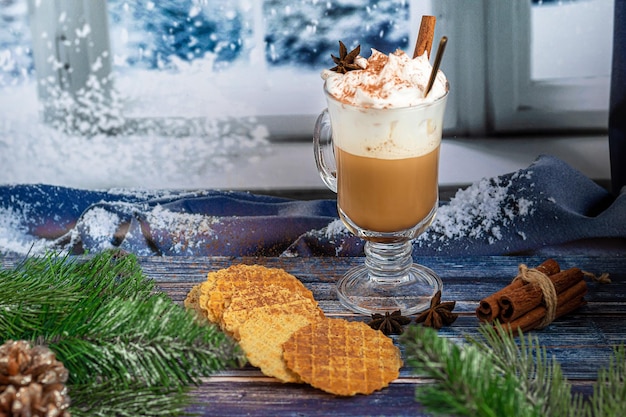 Café au lait chaud avec des bâtons de cannelle, saupoudré de cannelle. Décorations de Noël, branches d'un arbre de Noël. Concept de vacances Nouvel An. Sur un fond en bois.