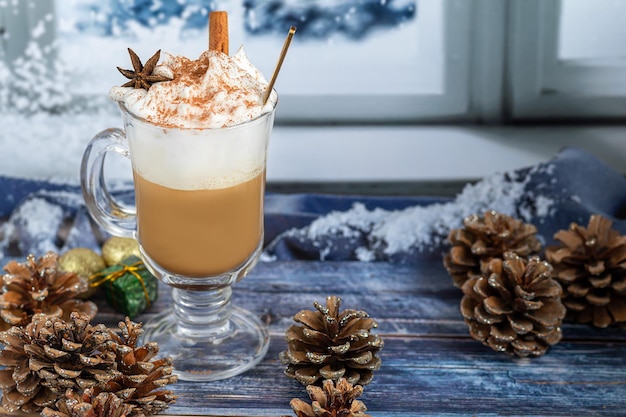 Café au lait chaud avec des bâtons de cannelle, saupoudré de cannelle. Décorations de Noël, branches d'un arbre de Noël. Concept de vacances Nouvel An. Sur un fond en bois.