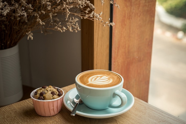 Café au lait chaud avec mousse de lait d'art latte dans une tasse et gâteau à la banane fait maison sur un bureau en bois sur la vue de dessus. Comme petit-déjeuner dans un café au café, pendant le concept de travail d'entreprise