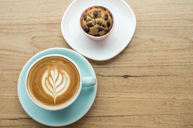 Café au lait chaud avec mousse de lait d'art latte dans une tasse et gâteau à la banane fait maison sur un bureau en bois sur la vue de dessus. Comme petit-déjeuner dans un café au café, pendant le concept de travail d'entreprise