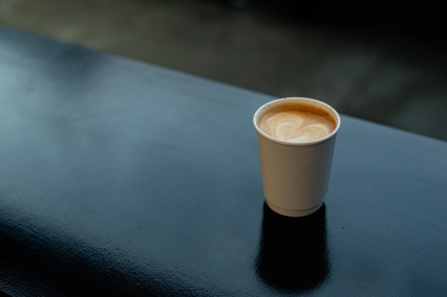 Un café au lait chaud servi dans une tasse en papier sur un tableau noir dans un café.