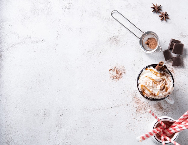 Café au lait avec crème au caramel crémeux, tube de papper rouge et cannelle dans une tasse blanche sur un tableau blanc. Vue de dessus et espace de copie