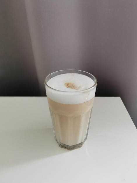 Café au lait fait maison avec du lait et de la mousse sur une table sur fond gris dans un bécher en verre