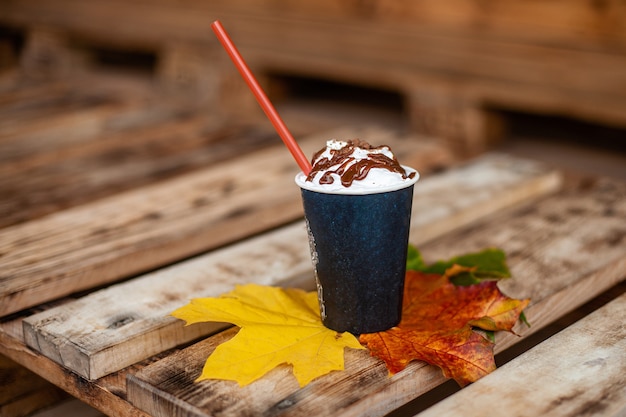 Café au lait avec de la paille sur les feuilles d'automne