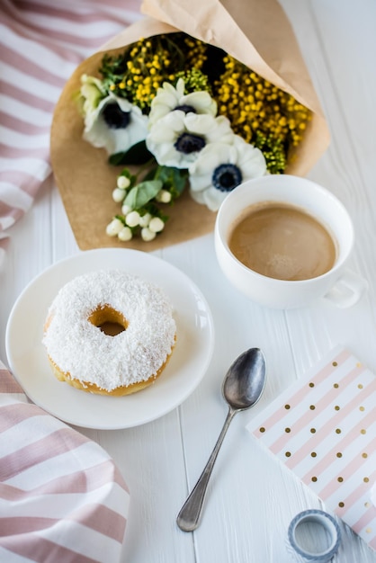 Café et un beignet avec des fleurs fraîches