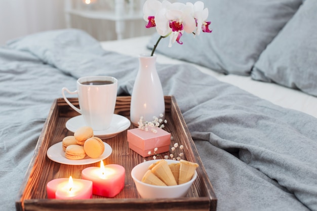 Café, bonbons, bougies, fleurs et girt sur un plateau en bois sur le lit. Concept avec Saint Valentin