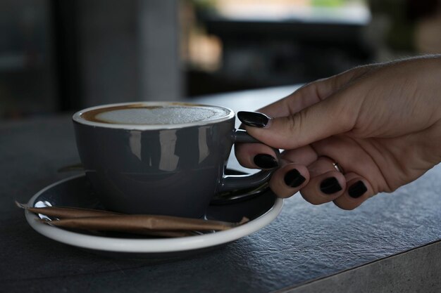 Photo un café cappuccino dans une tasse grise avec une soucoupe sur le comptoir du bar la main d'une femme prend une tasse