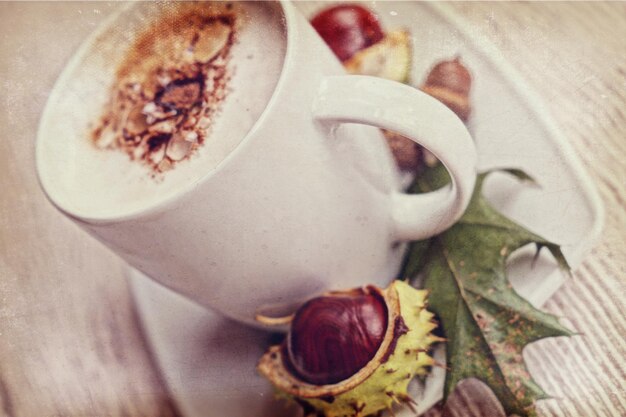 café chaud d'automne avec de la mousse et des châtaignes sur un fond en bois