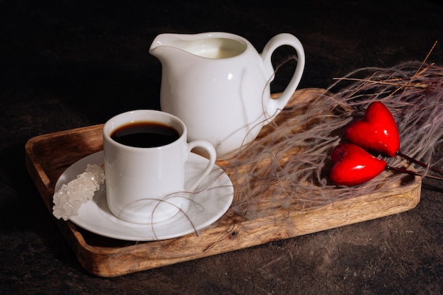 Café chaud dans une tasse de lait blanc et deux coeurs rouges sur un plateau en bois