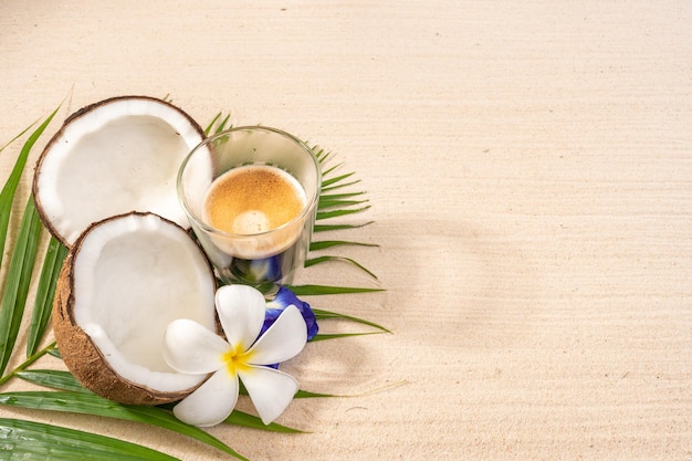 Café chaud et noix de coco sur feuille de palmier à la plage de sable.