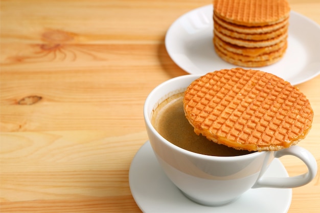 Café chaud avec Stroopwafel placé sur le dessus de la tasse avec une pile de Stroopwafel floue en toile de fond