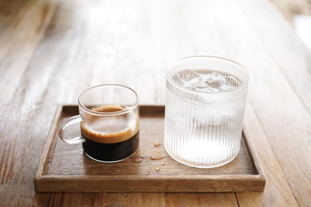 Café chaud et un verre de glace sur un plateau en bois sur une table en bois