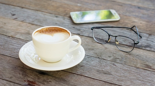 Café chaud, verres et smartphone sur une table en bois.