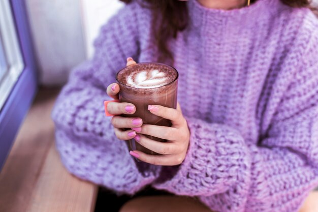 Café confortable. Femme en pull épais tricoté tenant un verre de cacao chaud avec des mains bien rangées avec des ongles roses