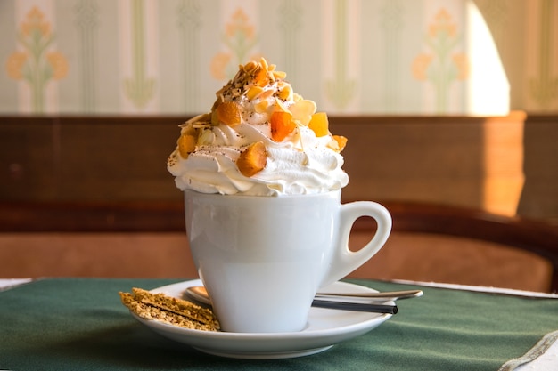 Café à la crème fouettée et fruits secs en tasse blanche sur une table dans un café avec un petit cookie