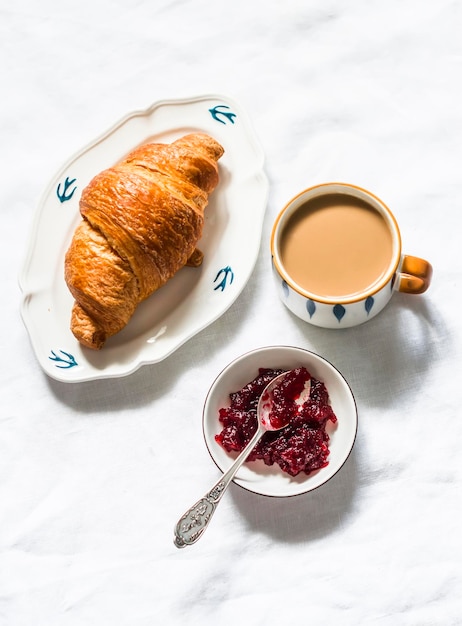 Café croissant avec confiture de canneberges à la crème sur une vue de dessus de fond clair