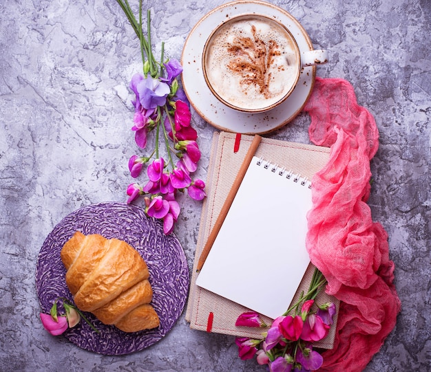 Café, croissants, fleurs et cahier.