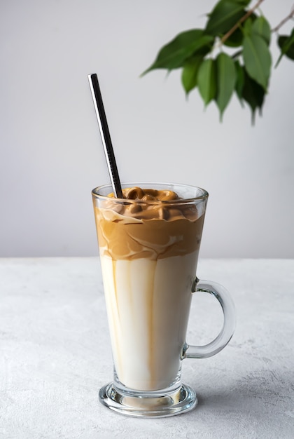 Café Dalgona dans un grand verre avec une paille sur un espace blanc