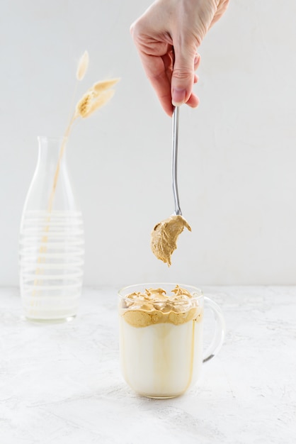 Café dalgona fouetté avec une cuillère à la main sur une lumière.