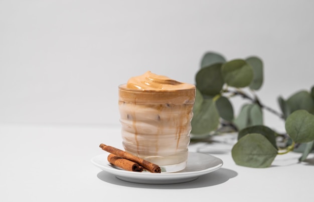 Café Dalgona fouetté avec du lait de soja Café froid instantané avec de la glace dans un verre avec des bâtons de cannelle sur un fond clair avec une branche Le concept d'une boisson à la mode et populaire
