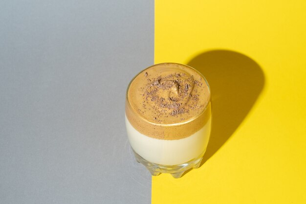 Café Dalgona avec mousse luxuriante dans un verre sur fond jaune et gris. Boisson coréenne tendance sur les couleurs Pantone tendances 2021.