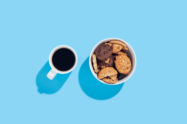 Café dans une tasse blanche biscuits dans un bol sur fond bleu