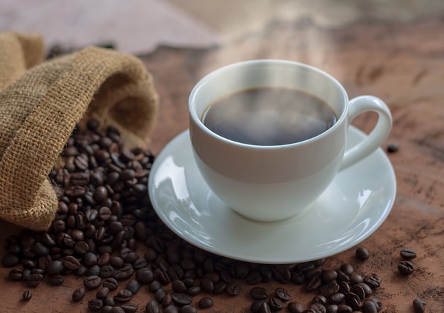 Café dans une tasse blanche et grains de café sur une table en bois