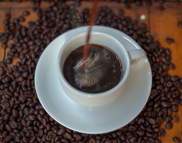 Photo café dans une tasse blanche et grains de café sur une table en bois