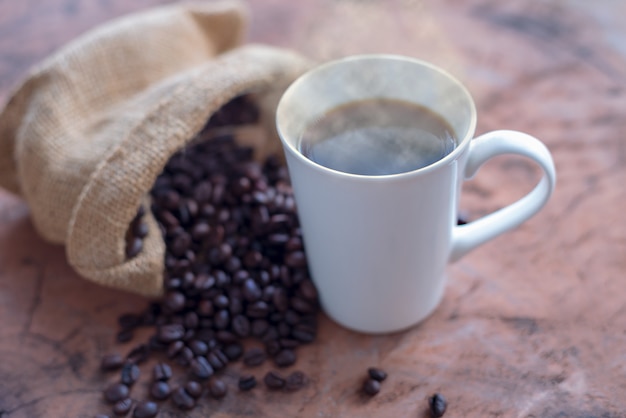 Café dans une tasse blanche et grains de café sur une table en bois