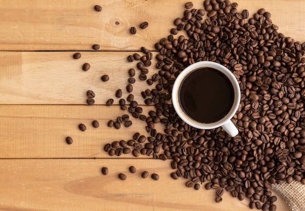 Café dans une tasse blanche avec des haricots sur une table en bois