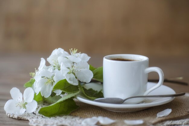 Café dans une tasse blanche sur une soucoupe blanche avec une cuillère à café et une branche d'un pommier fleuri