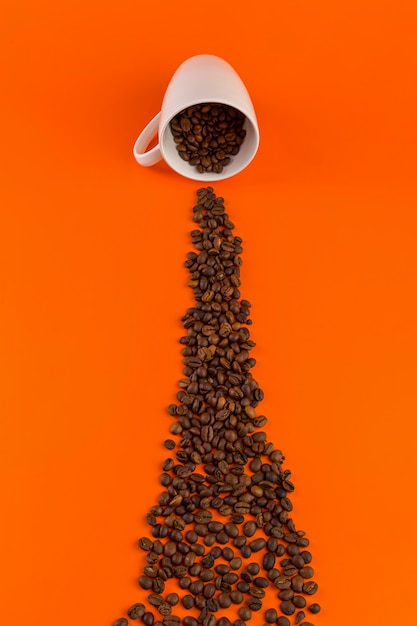 Café dans une tasse blanche sur une surface orange avec des grains de café.